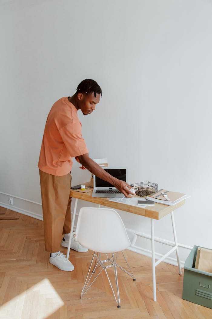 about-02 A man standing at a desk organizing papers and electronic devices in a modern office setting.